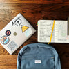 flat lay photography of blue backpack beside book and silver MacBook