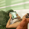 a woman laying on a couch holding a tablet