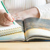 a person writing on a book with a pen