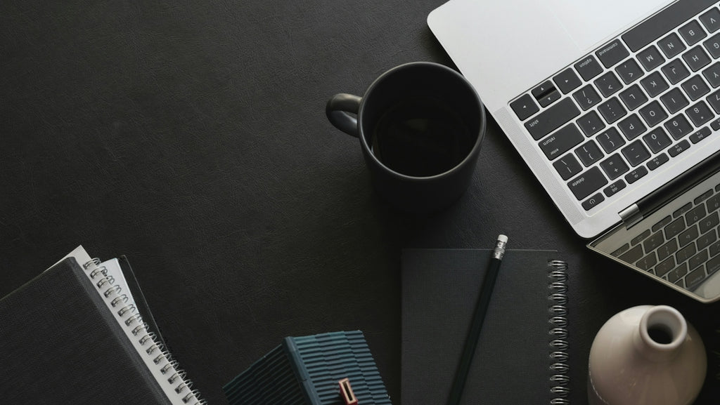Laptop, mug, and notebooks on a dark workspace