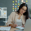 Woman working at a desk with laptop and notebook.