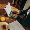 Woman typing on laptop at wooden table with breakfast.